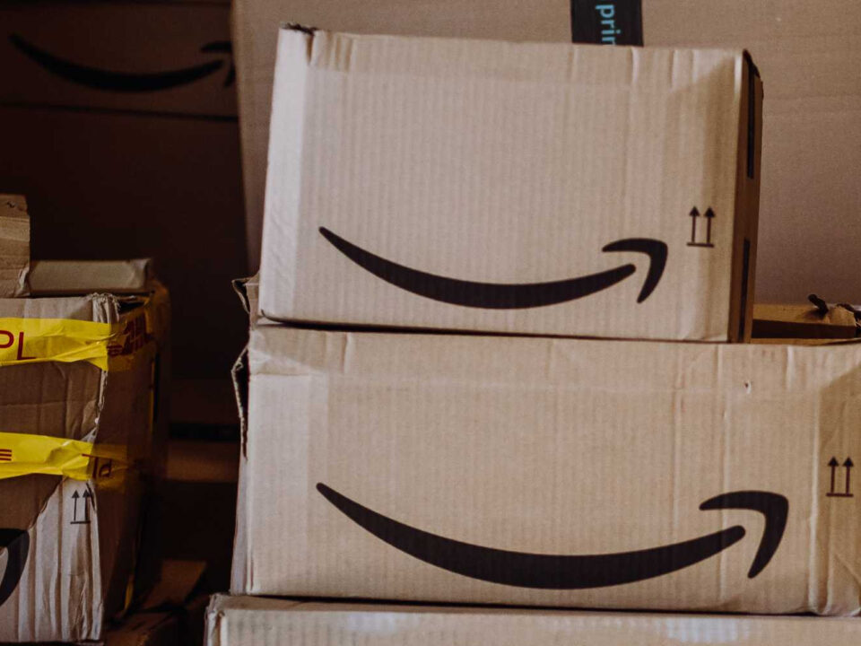 Stacked cardboard boxes with Amazon's smiling arrow logo and yellow tape, conveying a busy delivery or shipping environment.