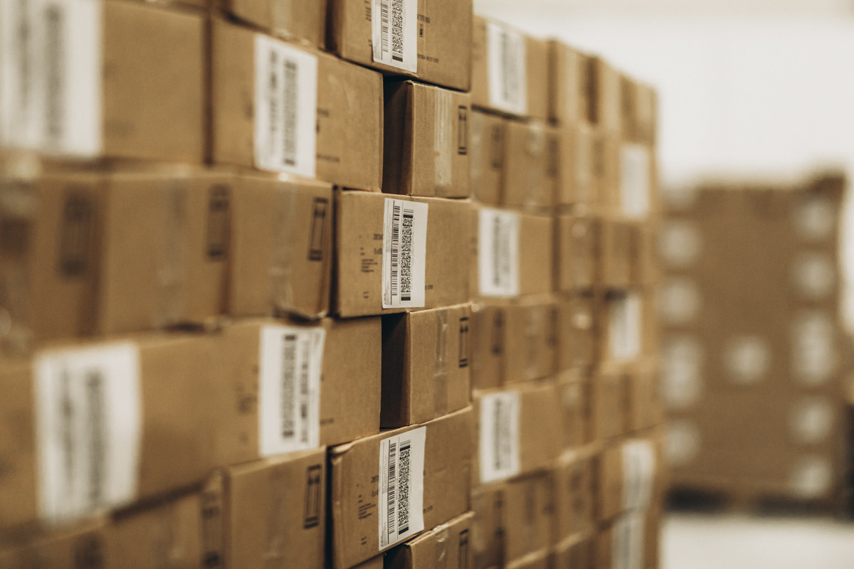 Rows of labeled cardboard cartons stacked in a warehouse storage area, with barcode labels visible on the front-facing boxes.
